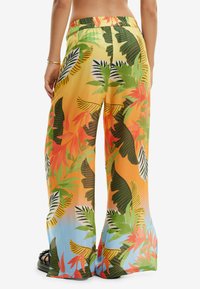 Szerokie spodnie wykonane z lekkiego materiału z wyrazistym tropikalnym nadrukiem. Kolory obejmują pomarańczowy, zielony i niebieski, z elastycznym pasem.