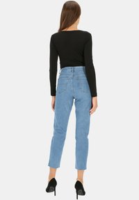 Czarna bluzka z długim rękawem w połączeniu z jasnoniebieskimi spodniami o wysokim stanie, mającymi prosty krój i dwie tylne kieszenie. Czarne szpilki.