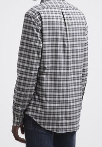 Camisa de manga larga a cuadros con pliegue en la espalda, hecha de mezcla de algodón. Los colores incluyen marino, verde y blanco. Detalles de botones visibles.