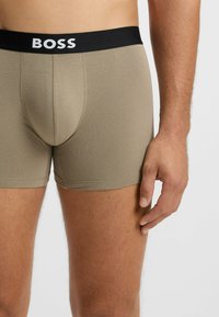 Beige Boxershorts mit einem schwarzen elastischen Bund, der das "BOSS"-Logo trägt. Der Stoff ist glatt und eng anliegend.