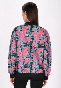 Kleurige bomberjack met een golvend roze, blauwe en zwarte print, voorzien van een zwarte ribgebreide kraag en manchetten op een zachte stof.