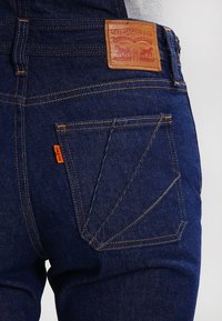 Dark blue denim jeans with a leather label reading "Levi Strauss & Co." on the back waistband and contrasting orange tab on the pocket.