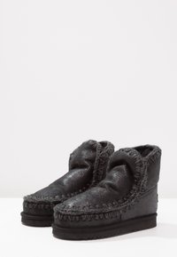 Zwarte suède enkelbotten met een zachte, textuurafwerking, voorzien van decoratieve stiksels en een luxe, opklapbare kraag.