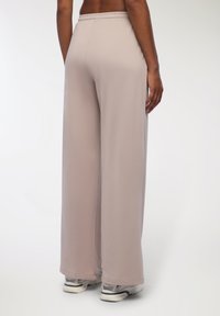 Jasne beżowe spodnie typu wide-leg z elastycznym pasem. Materiał wydaje się gładki i lekko połyskujący. Noszone z białymi i szarymi trampkami.