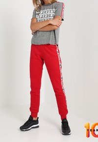 Grijze t-shirt met korte mouwen met "Superdry" tekstprint, gecombineerd met rode joggingsbroek met witte branding aan de zijkant en zwarte sneakers.