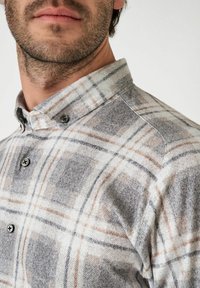 Hemd aus weichem, grauem Flanell mit einem karierenden Muster in Beige- und Schwarztönen. Abgeschlossen mit einem klassischen Kragen und schwarzen Knöpfen.