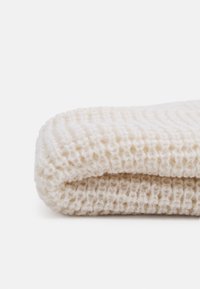 Krämfärgad stickad filt vikta, som har ett strukturerat, ribbat mönster med mjuka, plyschiga fibrer. Kanterna är rundade och släta.