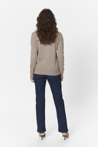 Beiger Pullover mit geripptem Saum, kombiniert mit dunkelblauen Jeans. Die Jeans haben am unteren Ende eine leichte Flared-Form und werden mit schwarzen High Heels getragen.