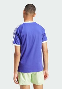 Fioletowa bawełniana koszulka z białymi akcentami na kołnierzu i rękawach. Posiada swobodny fason i miękką fakturę. Zestawiona z jasnooliwkowymi szortami.