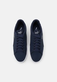 Granatowe buty sportowe z gładką cholewką, sznurowanym zapięciem, miękkim wnętrzem i białą gumową podeszwą. Charakteryzują się logo Puma na języku i boku.