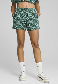 Shorts verts à motifs avec une taille à cordon, des poches latérales et une coupe décontractée, assortis à des chaussettes blanches et des baskets.