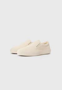 Slip-on kanvas sko i en lys beige farve med elastiske sideaccenter og en gummisål. Glat tekstur med minimalistisk design.