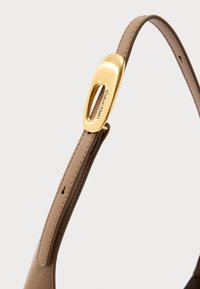 Calvin Kleini käekoti rihm helebeežist nahast, millel on siledapinnaline tekstuur ja kuldse tooniga metallist detail logoga. 