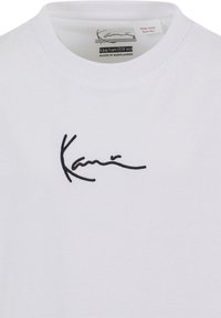 Hvitt t-skjorte med rund hals og korte ermer. Har en svart brodert signatur på forsiden. Laget av bomull.