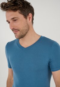 T-shirt a maniche corte con scollo a V in cotone blu, caratterizzato da una vestibilità aderente e una texture liscia. Design semplice senza motivi o accenti visibili.