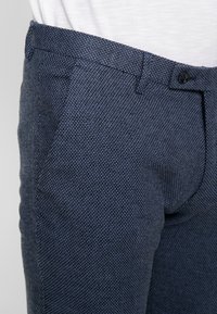 Navy blue textured trousers made from fabric with a small dotted pattern. Features a button closure and side pockets for practicality.