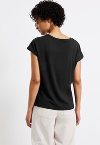 T-shirt nera in cotone con maniche corte arrotolate e scollatura ampia, con un design semplice e una texture liscia. Vista posteriore mostrata.