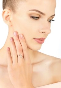 Silver ring with a v-shaped design and a small gemstone accent, worn on a hand touching the face. Skin tone is neutral, background is white.