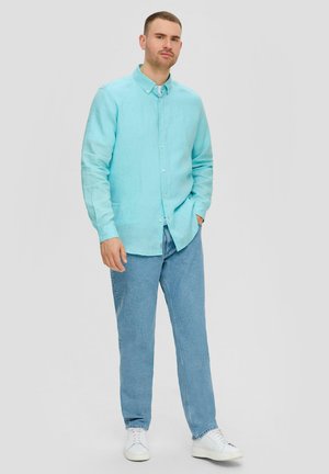 Lichtblauwe linnen overhemd met knopen en lange mouwen, gecombineerd met lichtblauwe spijkerbroek en witte sneakers. Eenvoudig, casual ontwerp.
