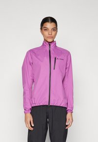 Giacca leggera rosa con colletto alto, zip completa, logo nero sul petto, polsini ed orlo elastici. Il modello indossa pantaloni neri.