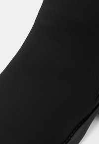 Bottine noire lisse avec un design élégant et un bout légèrement pointu, présentée sur fond blanc.