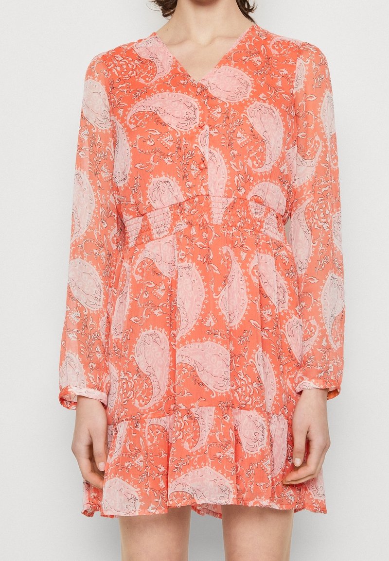 Kleid mit Korallen-Paisleymuster, transparenten langen Ärmeln, V-Ausschnitt und smocktem Taillenbereich. Ausgestellter Rock mit geschichteten Rüschen am Saum.