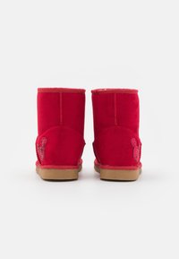 Bottines en daim rouge avec un bout arrondi, présentant un emblème décoratif de Mickey Mouse pailleté sur le côté et une semelle en caoutchouc beige.