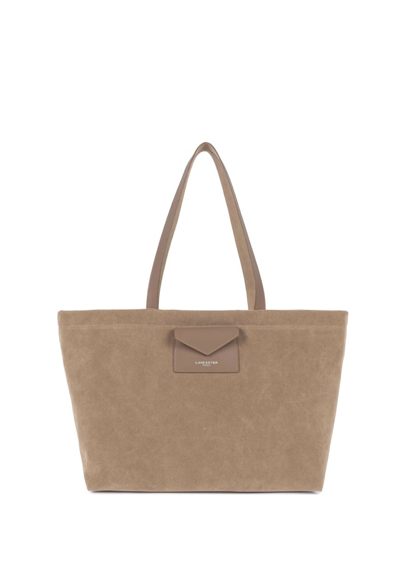 Borsa tote in camoscio beige con due manici lunghi, una tasca frontale con patta e dettaglio logo in rilievo. Forma rettangolare semplice con texture morbida.