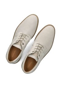 Lichtbeige veterschoenen met een bovenkant van gestructureerde stof, gladde leren accenten, bruine rubberen zolen en stikdetails langs de randen.