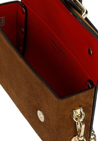 Sac à main en daim marron avec intérieur rouge, fermoir doré et bandoulière chaîne, ouvert montrant le nom de la marque à l'intérieur.