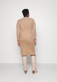 Beige geribbelde gebreide jurk met lange mouwen, knielang, met een ronde halslijn en textuurstof. Gecombineerd met lichtgekleurde knie hoge laarzen.