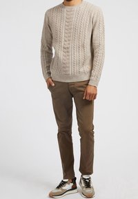 Beige-värinen kaapelineulepusero, jossa on teksturoitu kuvio, pyöreä kaula-aukko ja resorireuna, yhdistettynä ruskeisiin kapealahkeisiin housuihin ja monivärisiä yksityiskohtia sisältäviin lenkkareihin.