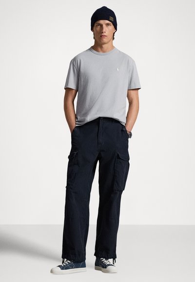 Grå t-shirt med rund hals, mörka cargobyxor med fickor och blåa tygskor. Bärs med en marinblå stickad mössa. Enkel, avslappnad stil.