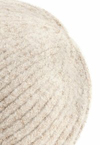 Chapeau rond en laine crème, avec un design texturé à côtes, présentant une surface douce et duveteuse avec une finition légèrement irrégulière.