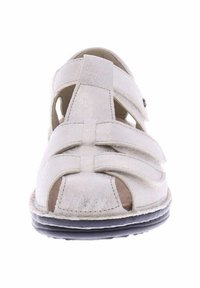 White leather sandal with open design. Features cross straps and cutouts. Textured upper, cushioned sole, black rubber outsole.