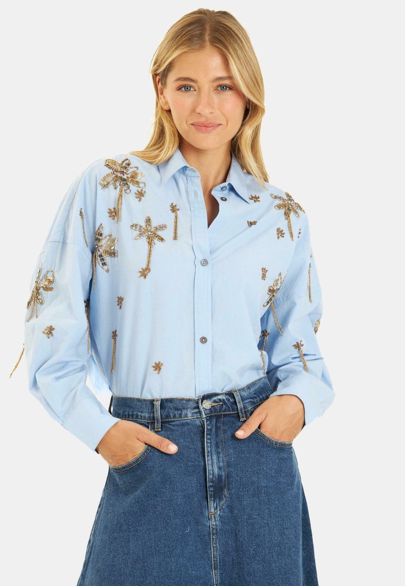 Lichtblauwe button-up shirt met gouden borduursels met palmboom- en bloemmotieven. Lange mouwen en een ontspannen pasvorm, gecombineerd met een spijkerrok.