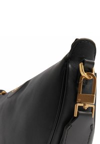 Sac à main en cuir noir à texture lisse, avec une fermeture en métal doré et une forme distinctement incurvée.