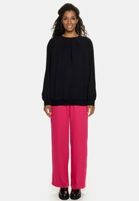 Czarna bluzka z długim rękawem i zgromadzonym dekoltem, zestawiona z jasnoróżowymi spodniami o szerokich nogawkach. Czarne buty na platformie dopełniają stylizację.