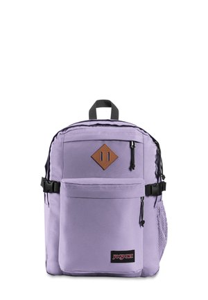 Lavendel Jansport rygsæk med sorte lynlåse, frontlomme, top håndtag, sidelomme i net, og en brun diamantformet patch på hvid baggrund.