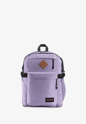 Lavendel Jansport rygsæk med sorte lynlåse, frontlomme, top håndtag, sidelomme i net, og en brun diamantformet patch på hvid baggrund.