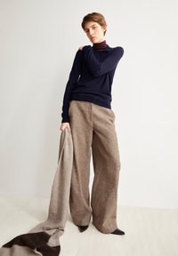 Marineblaues, langärmeliges Strickoberteil kombiniert mit braunen, strukturierten Hose mit weitem Bein und einem hellgrauen Schal, dazu spitze schwarze Schuhe.