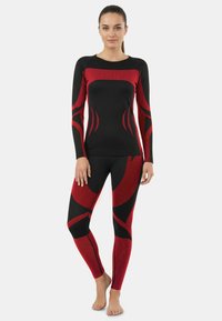 Black and red athletic set featuring a long-sleeve top with a fitted design and leggings with a bold, curved pattern. Smooth texture, stretchy material.