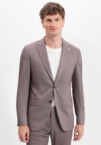 Braun gemusterter Anzug mit Revers und zwei vorderen Taschen, kombiniert mit einem weißen T-Shirt. Verfügt über einen Ein-Knopf-Verschluss.