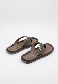 Chanclas marrones con una suela texturizada de color marrón oscuro, que presentan una tira a rayas y un pequeño acento metálico en la parte superior.