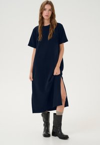 Abito a T-shirt in cotone blu navy con maniche corte, spacchi laterali e vestibilità comoda, abbinato a stivali alti neri in pelle.