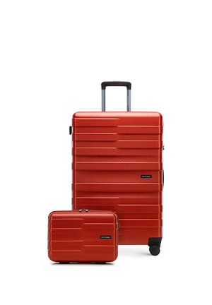 Červený kufr s tvrdým povrchem a vysouvací rukojetí a malá odpovídající příruční taška, oboje s vodorovnými texturovanými liniemi a černými kolečky.