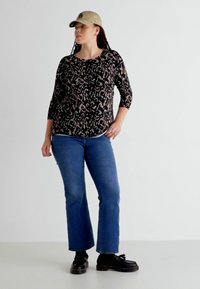 Svart och beige mönstrad långärmad topp, blå utsvängda jeans, svarta skor och en beige keps. Slät textur, avslappnad passform och avslappnad stil.
