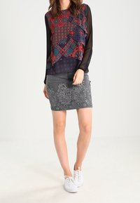 Blusa a maniche lunghe con motivo multicolore, abbinata a una gonna grigia ricamata. Sneakers bianche completano l'outfit.