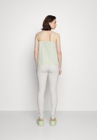 Camisola verde e branca com padrão xadrez, com alças finas, combinada com jeans skinny cinza claro e sapatos de plataforma verdes, vista de costas.