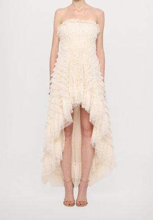Trägerloses, cremefarbenes Kleid mit asymmetrischem Saum, strukturierten Rüschen und mehrlagigem Tüll, kombiniert mit beigen Knöchelriemen-Pumps.